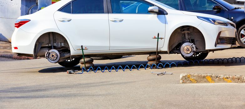 A white car without wheels stands on air jacks at a service station to replace tires.