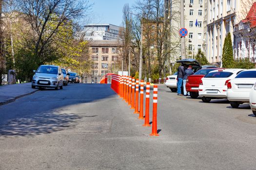 Orange reflective road columns bisect the road in the background of a city street, parking and standing cars under the bright spring sun.