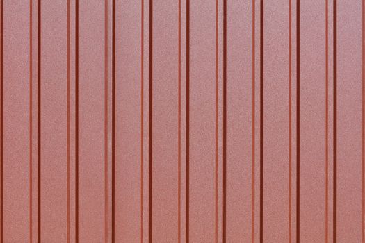 Brown metal fence made of corrugated steel sheet with vertical guides. Corrugated brown iron sheet background close up.