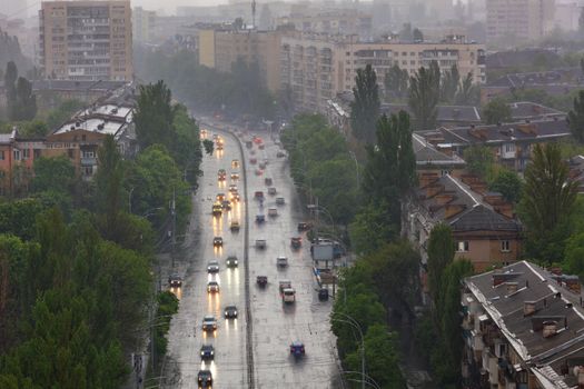 The lights of passing cars are blurred, their reflection on the wet road in heavy rain from a bird's eye view over residential areas and streets of the old city.