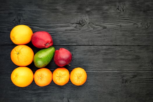 Oranges, tangerines, apples and avocados lie on an old black wooden surface, rustic style, flat lay, copy space.