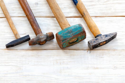 Old worn iron hammers with wooden handles are laid diagonally on a white wooden plank table, top view, copy space.