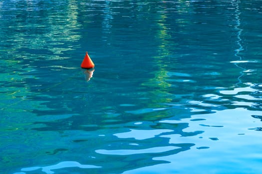 An orange buoy on the turquoise sea waves shows the direction of movement for marine boats and boats and a safe area for them.