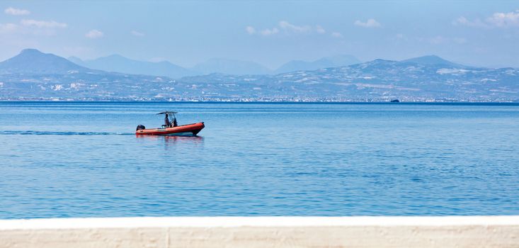 A small but fast rescue motor boat of red color, thanks to a powerful motor, can quickly come to the rescue, a lifeguard on duty patrols the coastline of the Greek coast of the Gulf of Corinth, an image with copy space.