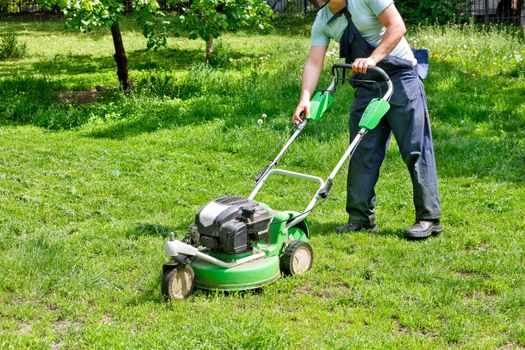 An industrial petrol, mower is ready to go and the gardener launches it to care for the green lawn in the city park, image with copy space.