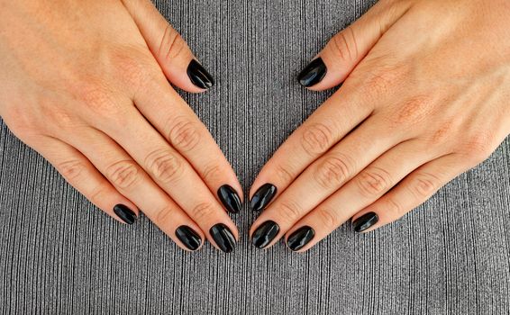 Beautiful female hands with beautiful french manicure nails, beautiful black with shine on a gray striped background textile.