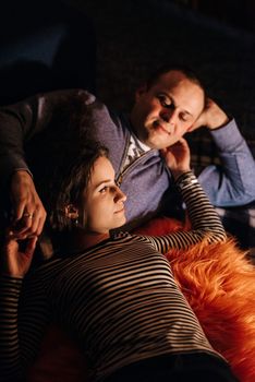 guy and girl are sitting in a wooden house on the background of a burning fireplace