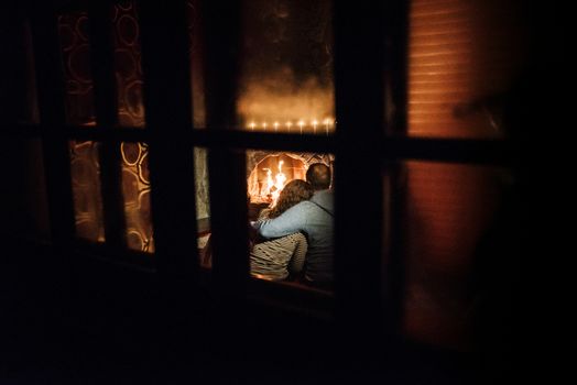 guy and girl are sitting in a wooden house on the background of a burning fireplace