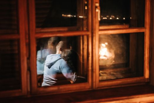 guy and girl are sitting in a wooden house on the background of a burning fireplace