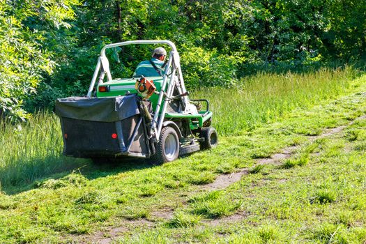 A professional tractor mower with increased cross-country ability under the control of an experienced gardener, climbs the grassy slope and mows tall grass.