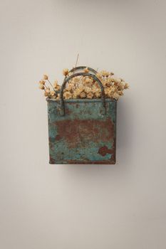 Bunch of tinny artificial flowers, hay colored, inside a blue metal box, very old and rusted, hanging on the wall