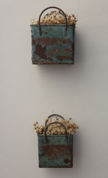 Bunch of tinny artificial flowers, hay colored, inside two blue metal boxes, very old and rusted, hanging on the wall