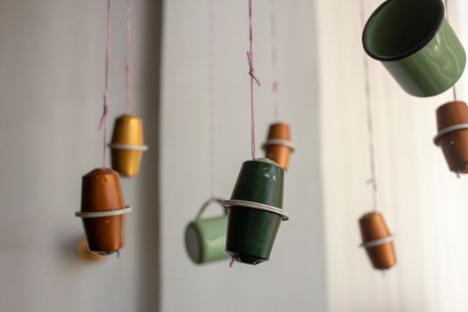 Handcrafted piece of decoration made of used coffee capsules and metal cups, hanging by wool threads