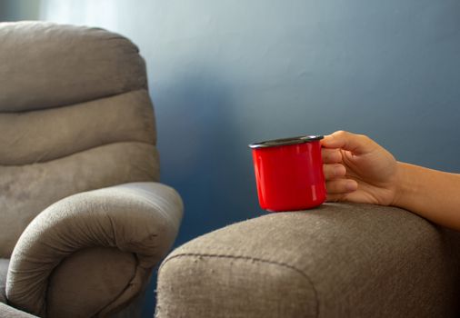 Woman holding a red metal cup resting her hand on the sofa's arm, next to a couch