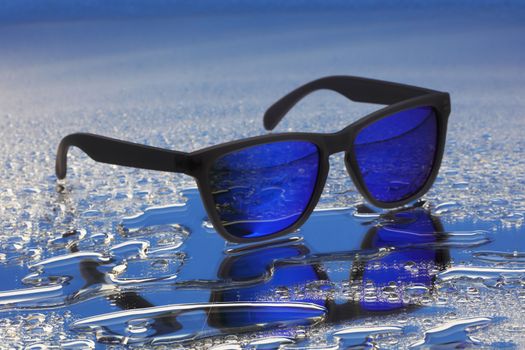 Blue sunglasses with black frames on water droplets reflection with selective focus
