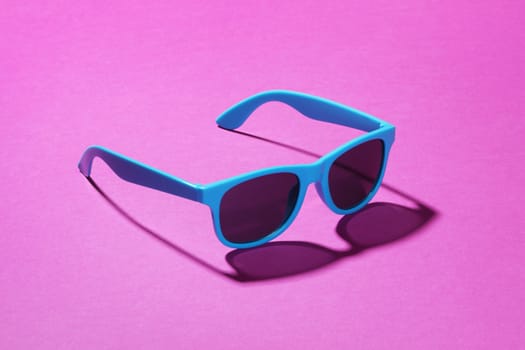 A pair of blue sunglasses on a pink background with shadow