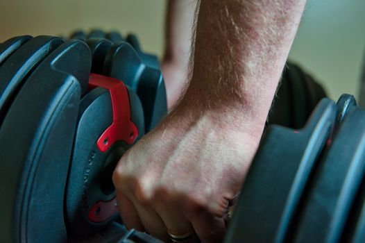 Hand gripping adjustable dumbbells for working out at home. male hand with ring visible.