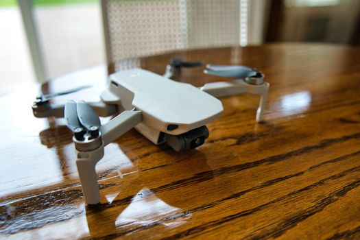 Drone sitting on wooden table inside on sunny day. Door visible in background.