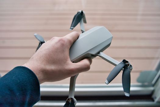 Hand holding drone with wooden deck visible in background. White man's hand grasping small flying drone preparing it to take off.