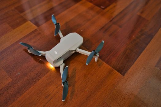 Drone sitting on wooden floor with light on indicating dead battery. Indoor drone flying.