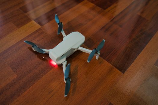 Drone sitting on wooden floor with light on indicating dead battery. Indoor drone flying.