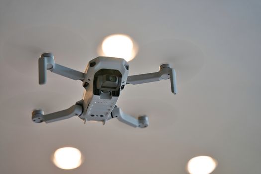 Drone flying indoors with ceiling visible in background. Underside of drone in flight inside of house.