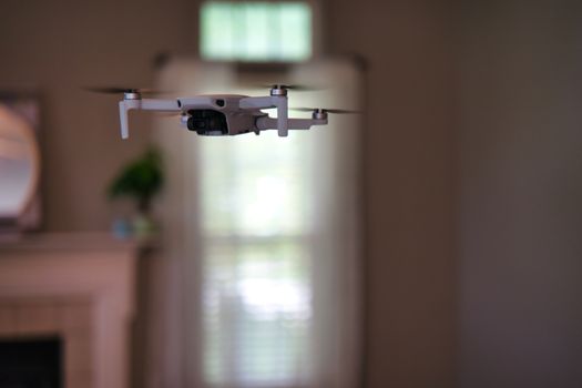 Drone flying indoors with window visible in background. White drone hovering inside of house.