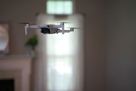 Drone flying indoors with window visible in background. White drone hovering inside of house.