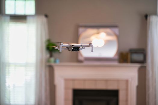 Drone flying indoors with window visible in background. White drone hovering inside of house.