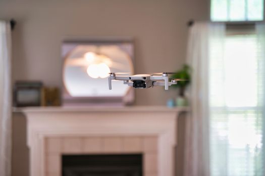 Drone flying indoors with window visible in background. White drone hovering inside of house.