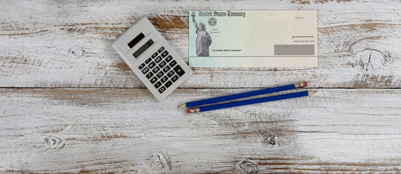 Economic impact stimulus check on white wooden desktop with pencils and calculator. 