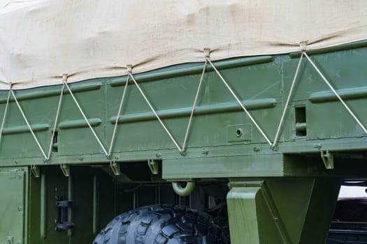 side of a dark green military truck with an awning secured with a cord