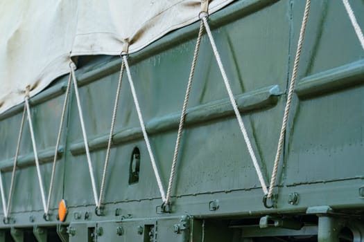 side of a dark green military truck with an awning secured with a cord