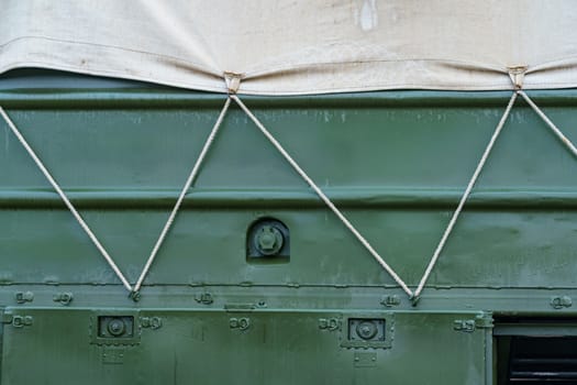 side of a dark green military truck with an awning secured with a cord