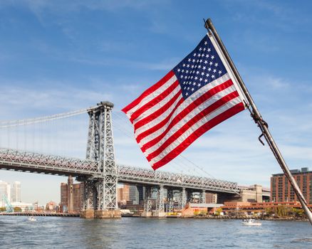 An American flag flies from a boat on the East River in New York City.  In the background is the Williamsburg Bridge connecting Manhattan and Brooklyn.