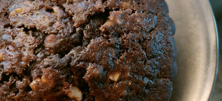 An extreme close up of hot and big chocolate walnut muffin on a steel plate on a weave pattern table