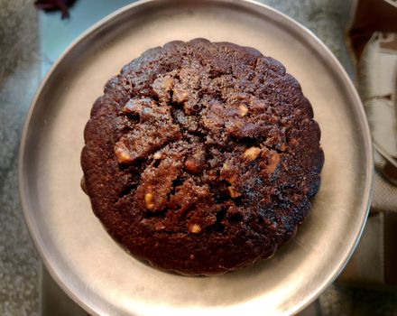 A chocolate walnut muffin on a steel plate in yellow light in a square composition