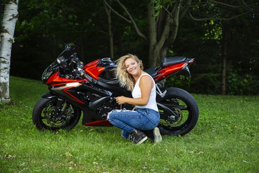 Young blond woman, kneeling beside a sport motocyle