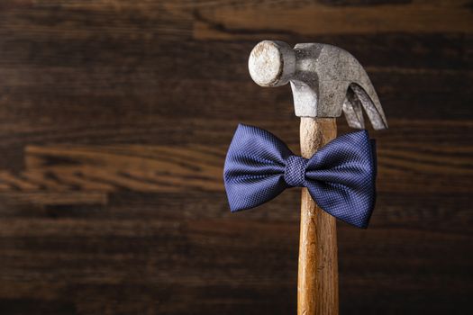 Old banged up hammer with a blue bowtie against a wood background
