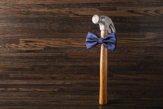 Old banged up hammer with a blue bowtie against a dark wood background