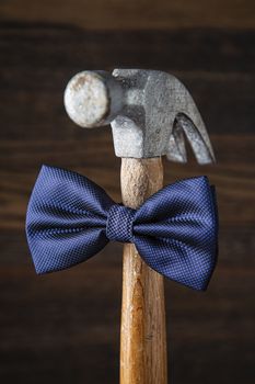Portrait of an old banged up hammer with a blue bowtie against a dark wood background
