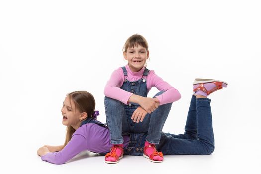 Happy girl sits on her sister's back in a white background