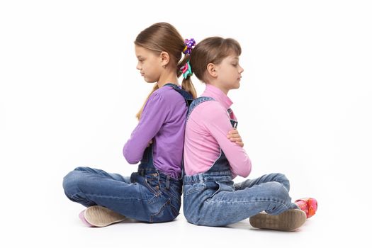 Two quarrelled girls sit with their backs to each other on a white background