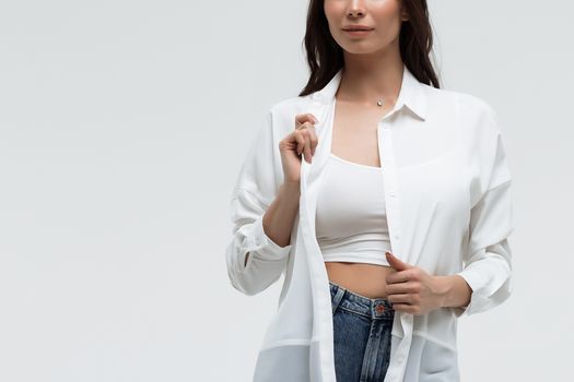 Crop confident long haired woman in white shirt and lingerie and jeans with crossed hands on white background