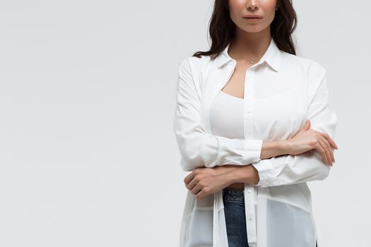 Crop confident long haired woman in white shirt and lingerie and jeans with crossed hands on white background