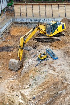 A large yellow excavator digs a foundation pit at a new construction site, viewing angle from a height, vertical image, copy space.