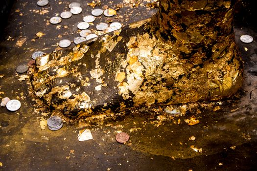 Golden leaf taped and Thai bath coin on the Buddha foot statue