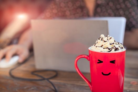 hot mocha coffee in red cup with smile face on wooden table with working man using laptop