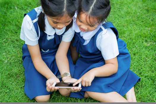 two little sister girls playing internet with mobile smartphone on grass