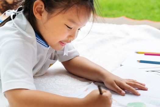 cute little girl writes to writing-books. The decision of lessons. girl lay down drawing the picture
